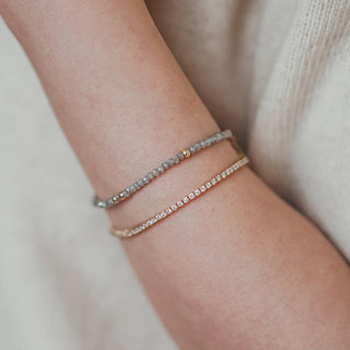 Arm showing grey raw diamond bracelet alongside a yellow gold diamond tennis bracelet.