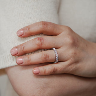 Hand with diamond set wedding band on cross-armed woman wearing a sweater dress.