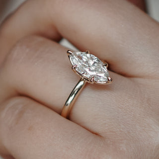 Close up of marquise solitaire on yellow gold band on hand.