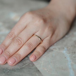 Hand with plain engraved band sitting on marble table.