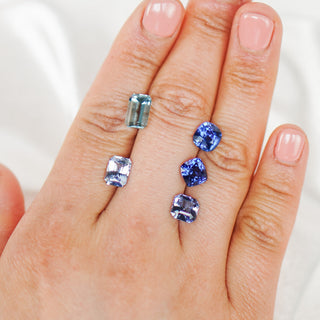Hand showing loose blue sapphires and aquamarines. 