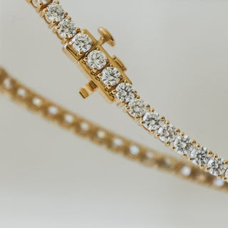 Close view of round brilliant lab grown diamonds set in yellow gold tennis bracelet links, box clasp above the line of stones.