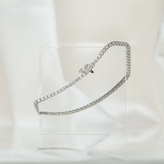 Natural Diamond tennis bracelet in white gold resting on an acrylic block, prong set round brilliant stones.