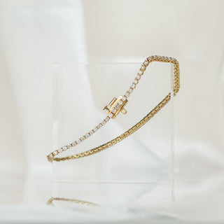 Yellow gold natural Diamond tennis bracelet draped over a clear acrylic block, round brilliant stones with box clasp visible.