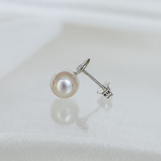 A single pearl stud earring with a silver post and butterfly back, resting on a white textured surface with a soft reflection.