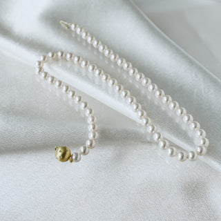 A delicate strand of white pearls draped elegantly on a soft white satin fabric, featuring a small gold bead accent and a gold clasp.