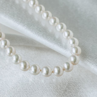 A strand of white freshwater pearls draped elegantly on a soft, white satin fabric background.