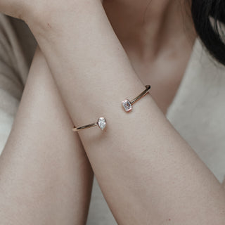 Yellow gold toi et moi bangle worn on the wrist, bezel set lab diamonds meeting at the gap against a white top.