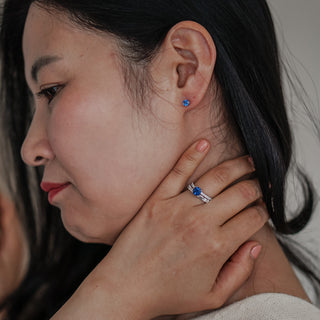 Close-up of a woman wearing a blue gemstone earring and ring, with a blurred background.
