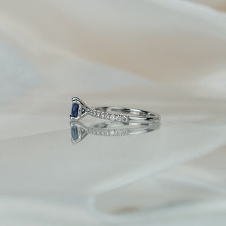 Side view of a cushion blue Sapphire engagement ring, four-prong basket and pavé stones along the shank.