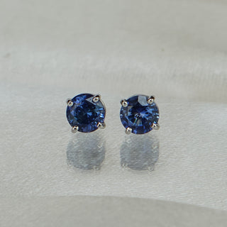 Pair of natural blue Sapphire round brilliant studs facing forward, matched color on a pale background.
