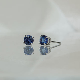 Natural blue Sapphire stud earrings in 14k white gold, round brilliant stones in four-prong settings with reflection below.