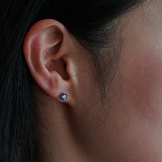 Blue Sapphire stud earring worn on the ear, 4.5mm round stone in a white gold four-prong setting.