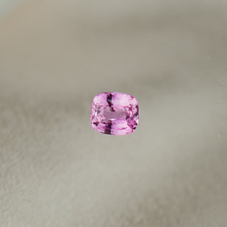 A single cushion-cut pink gemstone with dark inclusions, centered on a soft, light beige textured background.
