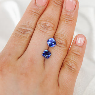 A close-up of a person's hand displaying a pair of small blue gemstone stud earrings.