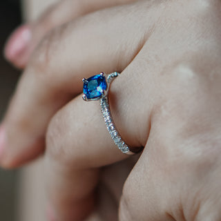 Natural cushion cut blue Sapphire ring worn on the hand, cornflower blue center above a Diamond set band.