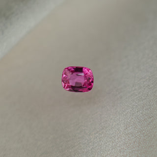 A single cushion-cut pink gemstone, likely a tourmaline, centered on a textured light beige fabric background.