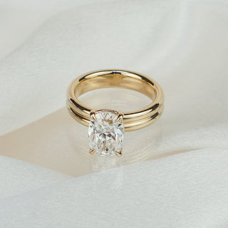 Cushion cut lab grown diamond solitaire in yellow gold on satin fabric, four-prong center over a chunky double shank.