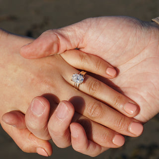Cushion cut solitaire engagement ring worn while holding hands, double shank in yellow gold catching light.