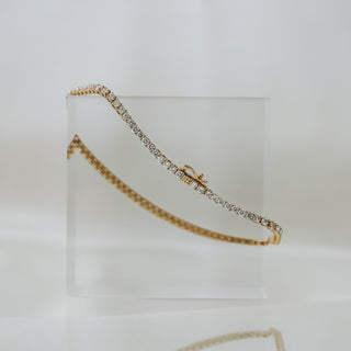 Lab diamond tennis bracelet in yellow gold draped over a clear acrylic block, continuous stone line against a neutral backdrop.