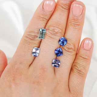 Hand holding five blue gemstones of different shapes and sizes on a white background