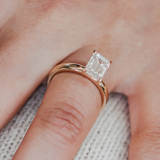 Lab grown diamond pipe shank engagement ring worn on the hand, emerald cut center above the rounded band.