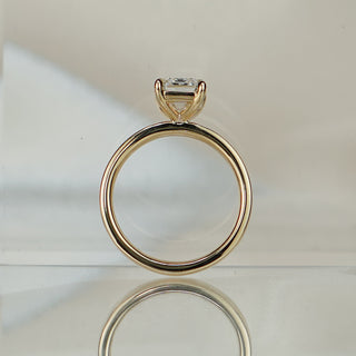 Emerald cut lab diamond pipe shank ring standing upright with reflection, four prongs above the round-profile band.
