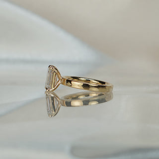 Side view of an emerald cut pipe shank engagement ring, the tubular band meeting the corner prongs in yellow gold.