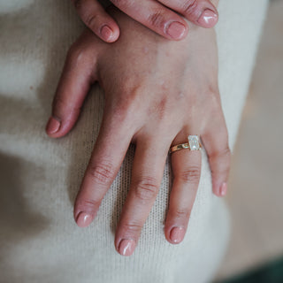 Emerald cut solitaire engagement ring worn on the hand, substantial pipe shank in yellow gold.