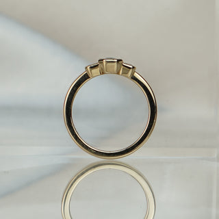 Emerald cut teal Sapphire engagement ring standing upright with reflection, three bezel set stones across the top.