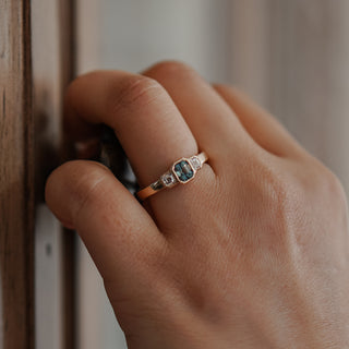 Teal Sapphire three-stone engagement ring worn on the hand, bezel set stones on a substantial yellow gold band.