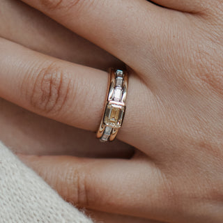 Two-tone triple shank engagement ring worn on the hand, emerald cut yellow Diamond in a bezel between bar-set baguettes.