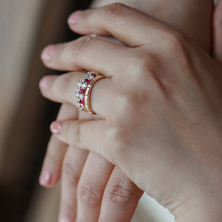 Yellow gold faceted band worn stacked on the hand with a colored stone ring, geometric panels visible in close view.