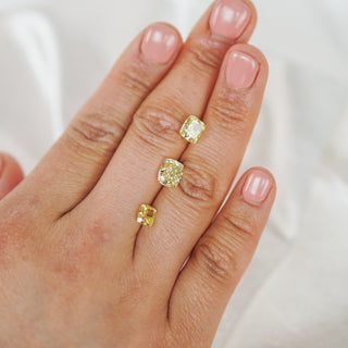 Hand wearing three gold rings with gemstones on a neutral background