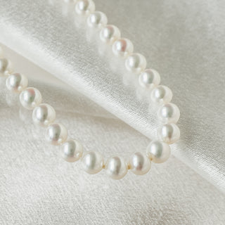 A strand of white freshwater pearl beads draped elegantly on a textured white fabric background.