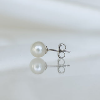 A single pearl stud earring with a silver post and butterfly back, displayed on a reflective white surface.