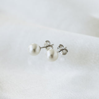 Freshwater pearl stud earrings in 14k white gold on soft white fabric, round pearls with friction back posts visible.