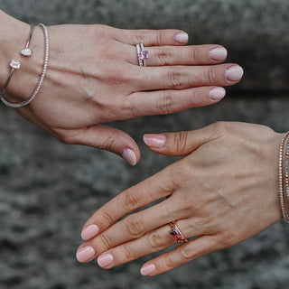 Two hands with sapphire engagement rings and bracelets against the street.