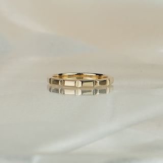 Side view of a 14k yellow gold faceted wedding band, geometric panel edges visible along the exterior.