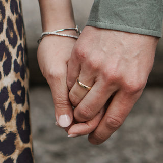 Couple holding hands, one wearing a men's gold wedding band.