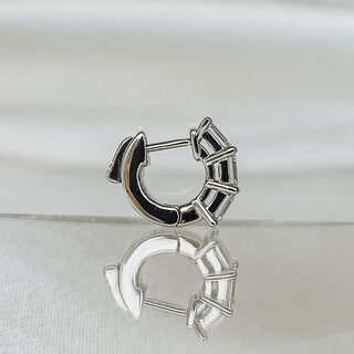A silver crescent-shaped huggie hoop earring with a black enamel inlay, displayed on a reflective white surface.