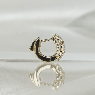 A gold huggie hoop earring with a crescent moon design and a row of clear stones, displayed on a reflective white surface.