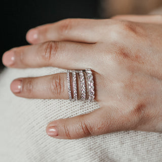 Hand wearing three diamond rings on a neutral background