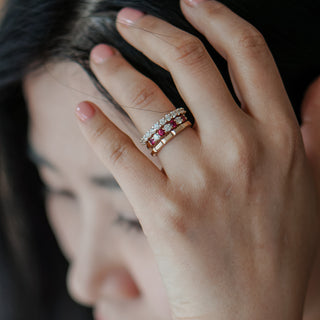 Close-up of a hand wearing two rings with red gemstones, blurred background