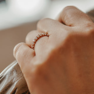 Rose gold shared prong lab diamond band worn on the hand, slim stone row catching light.