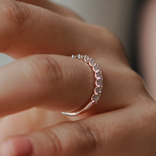 Shared prong wedding band with round lab grown diamonds held at the fingertips, rose gold claws visible between stones.