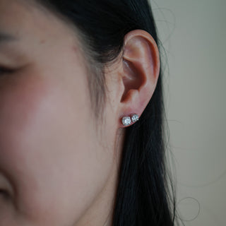 Round brilliant lab diamond stud worn on the ear in profile, white gold four-prong setting catching light.