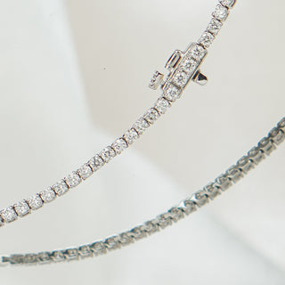 White gold tennis bracelet with round brilliant lab grown diamonds, strand curving with safety clasp visible.