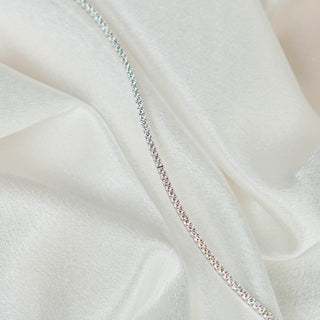 White gold lab diamond tennis bracelet resting along a fold of ivory satin, thin stone line in soft light.