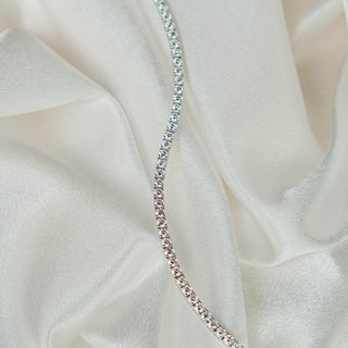 White gold natural Diamond tennis bracelet draped on ivory satin, stone line catching light along the curve.